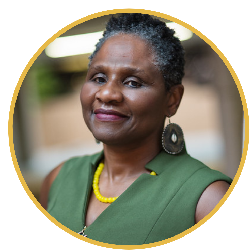 Licensed Clinical Therapist Jacqueline Samuda is a black woman with short natural black and gray hair, dark brown skin, brown eyes, red lipstick. She is wearing a green dress and yellow pearls.